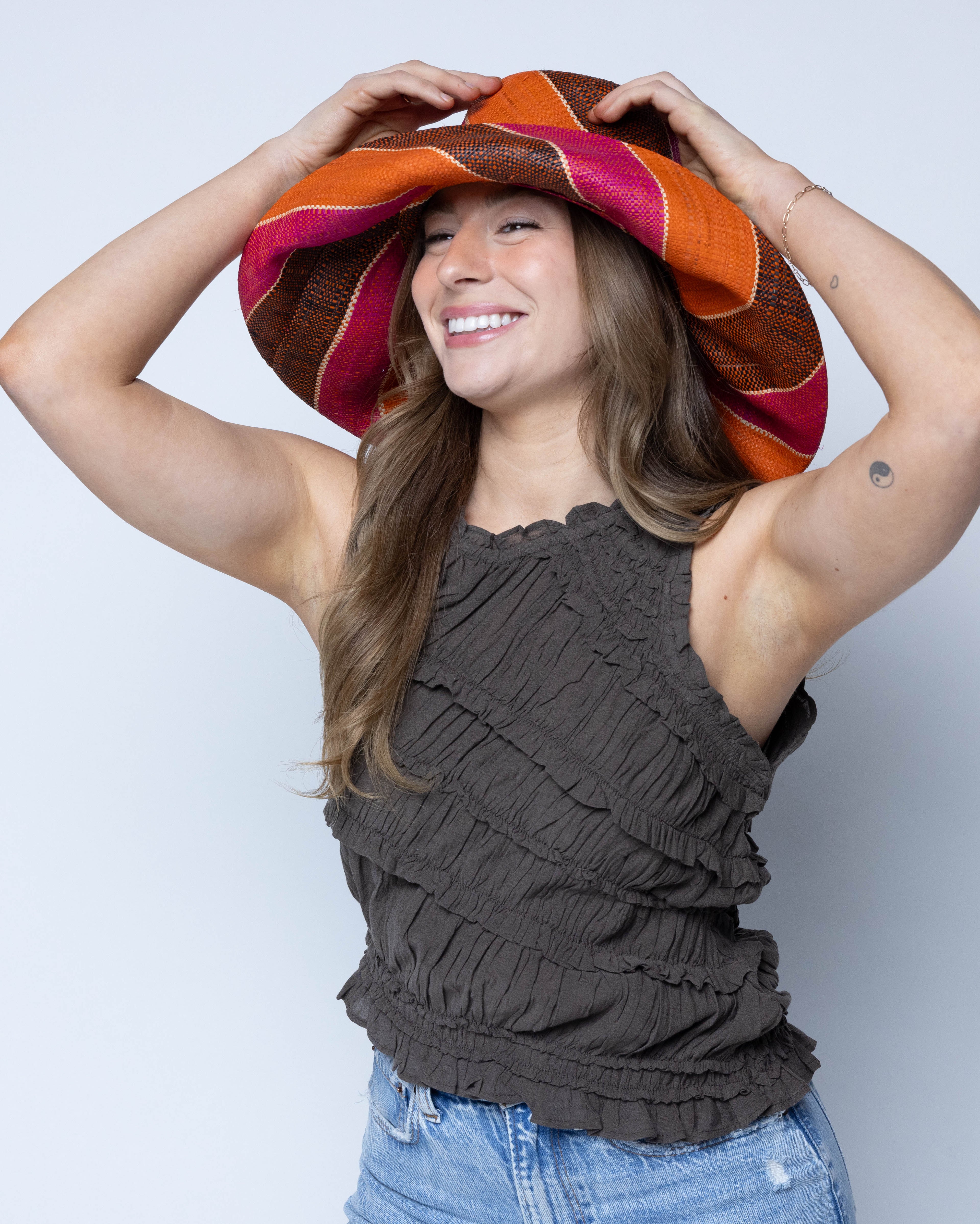 Model wearing Monica 5" Wide Brim Whimsy Swirl Multicolor Stripes Packable Straw Sun Hat Handmade loomed raffia in multi width bands of coral orange, fuchsia pink, black, natural straw color, etc. create a swirl pattern - Shebobo