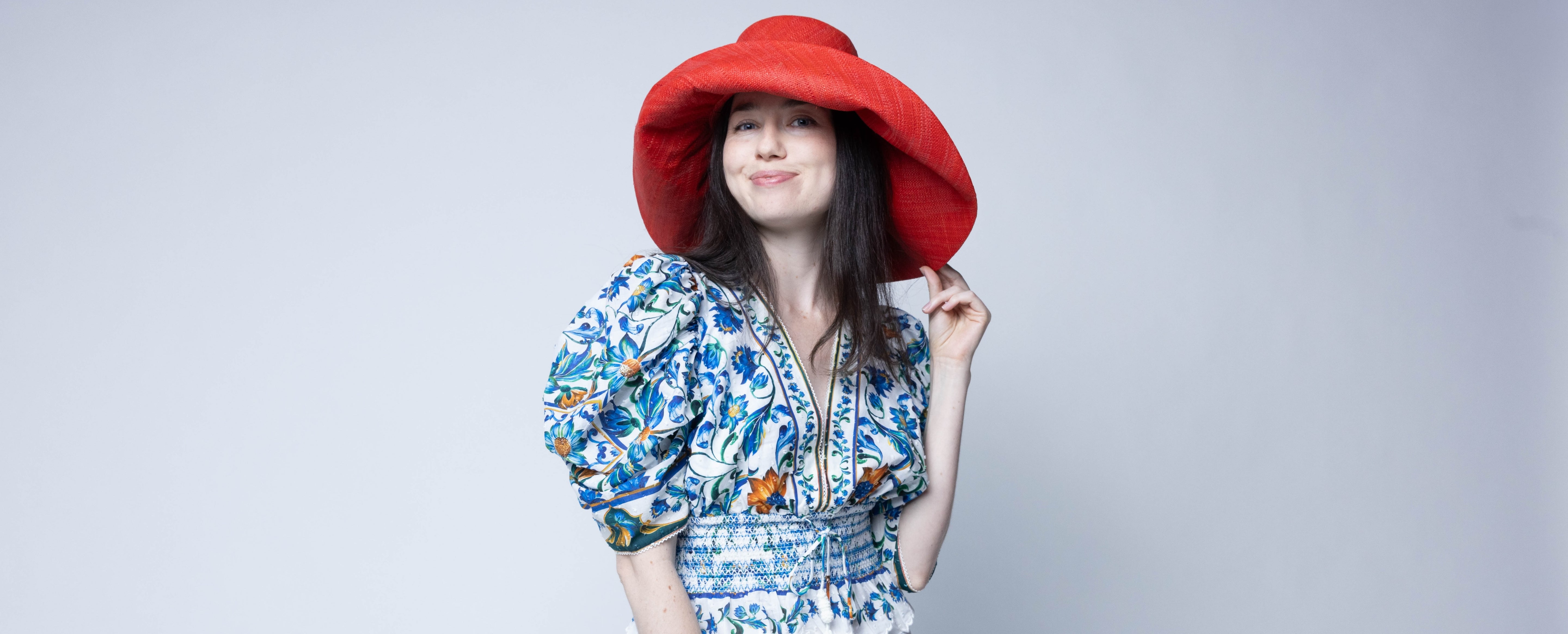 Model wearing Monica 7" Wide Brim Coral Solid Color Packable Straw Sun Hat handmade loomed raffia in a solid hue of coral orange/red  - Shebobo