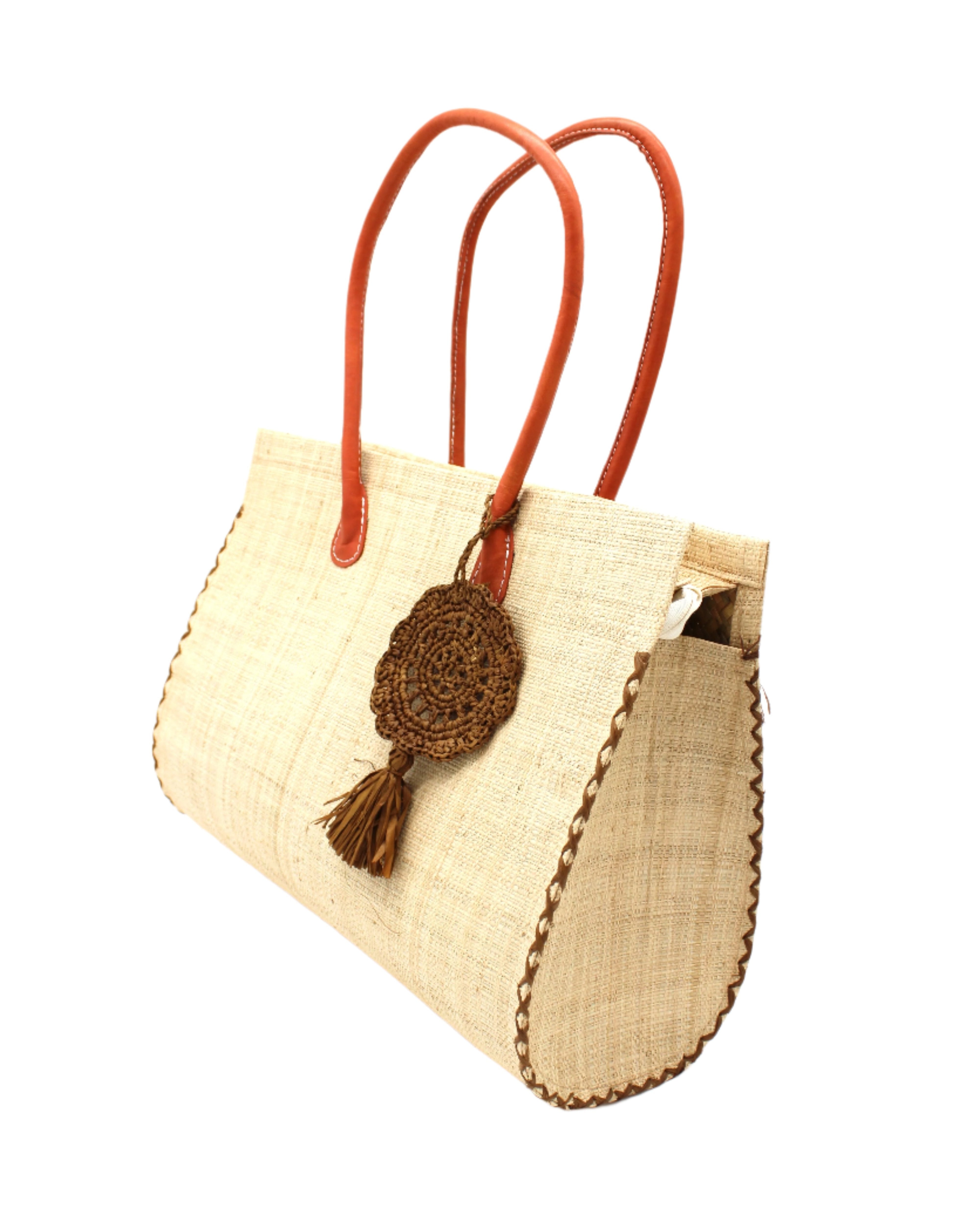 Side View Monte Carlo Big Straw Beach Bag with Dreamcatcher Tassel Charm Embellishment handmade loomed raffia palm fiber in a solid hue of natural straw color with contrasting crosshatch stitch edging in cinnamon/tobacco/dark/brown with matching crochet dreamcatcher disc and tuft tassel charm embellishment and leather handles oversized large handbag shoulder bag - Shebobo