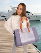 Model wearing Monte Carlo Wynwood Big Straw Beach Bag with Metallic Detailing Denim Shoulder Bag handmade loomed raffia palm fiber in a solid hue of denim retro/light blue with incorporated woven in vegan leather silver metallic strands and leather handles purse - Shebobo