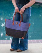 Model wearing Monterey Two Tone Denim and Black Straw Tote Bag handmade loomed raffia fibers in a color block pattern of denim retro/light/blue colored upper half, and black lower half - Shebobo