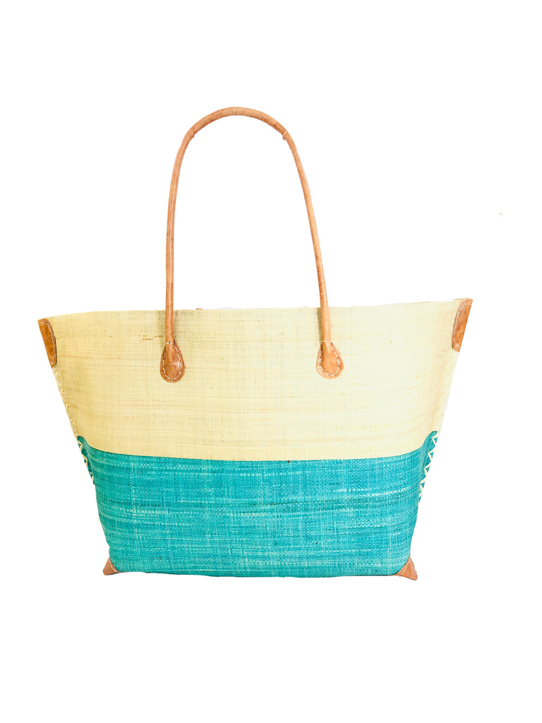 Model wearing Monterey Two Tone Straw Tote Bag handmade loomed raffia fibers in a color block pattern of natural straw colored upper half, and seafoam blue/green lower half - Shebobo