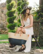 Model wearing Monterey Two Tone Straw Tote Bag handmade loomed raffia fibers in a color block pattern of natural straw colored upper half, and black lower half - Shebobo (with 5" Wide Brim Packable Black Stripes Multicolor Straw Sun Hat)