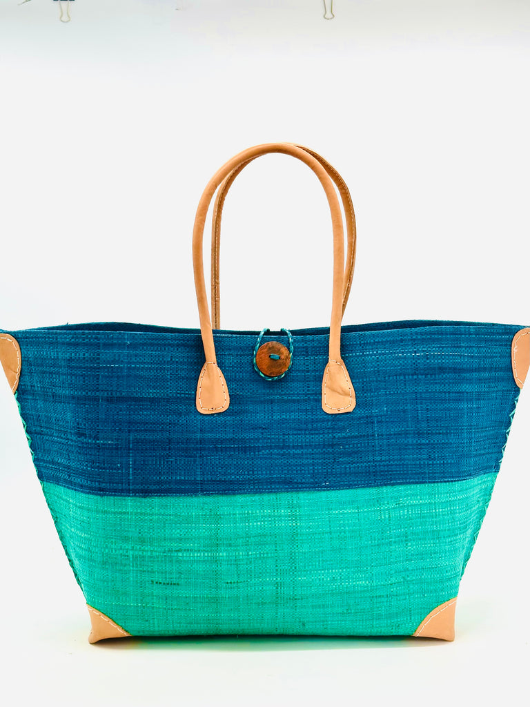 Model wearing Monterey Two Tone Straw Tote Bag handmade loomed raffia fibers in a color block pattern of turquoise blue colored upper half, and seafoam blue/green lower half - Shebobo