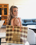Model wearing Nador Gingham Zippered Straw Bag in two tone cinnamon/tobacco/brown and natural straw color plaid pattern handbag handmade from loomed raffia palm shopping tote that packs flat with zipper closure and leather handles beach bag purse - Shebobo