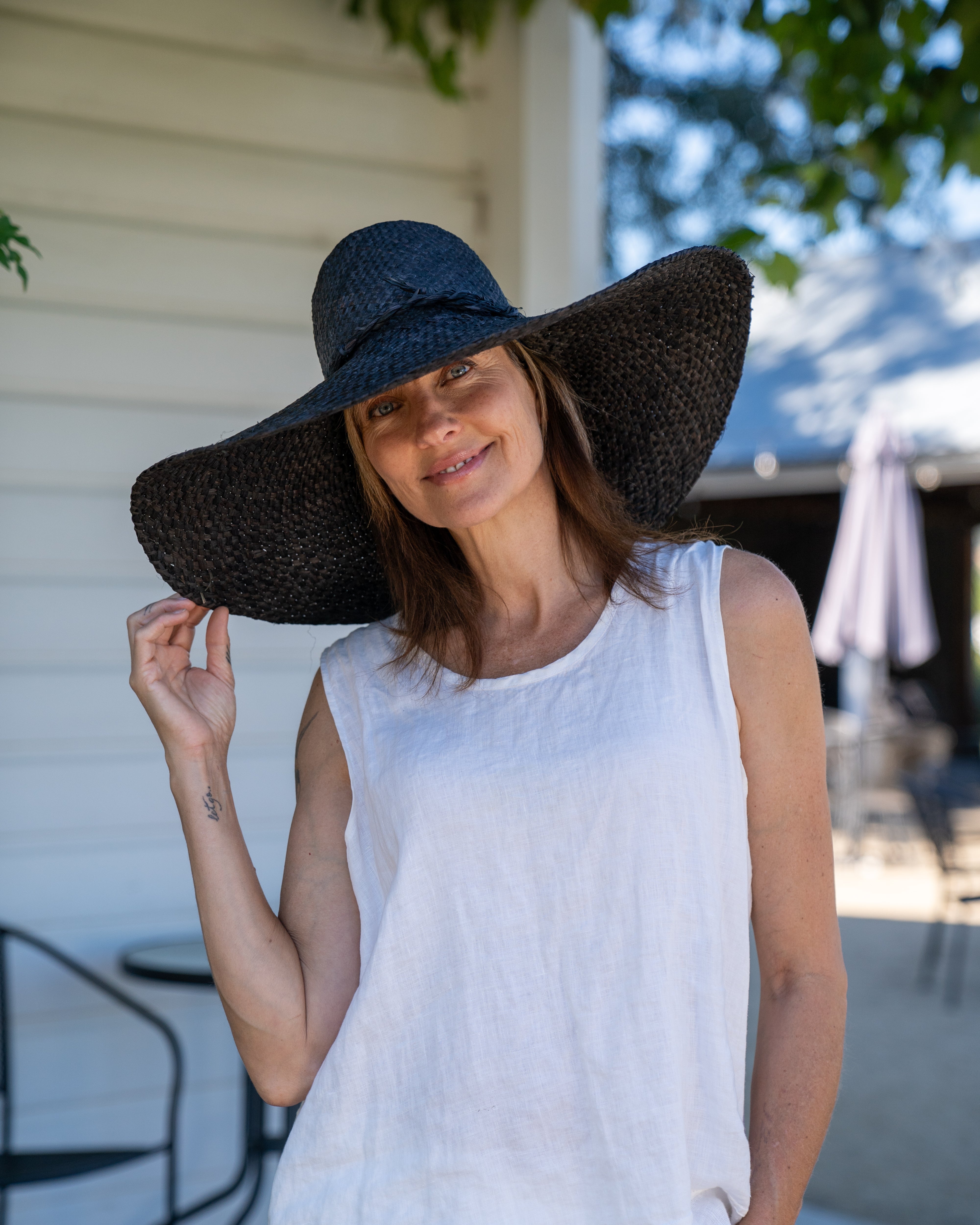 Model wearing 7" Wide Brim Natasha Black Woven XL Straw Sun Hat handmade woven natural raffia palm fiber in a solid hue of black with matching adjustable twisted raffia hat band and and extra wide brim - Shebobo