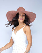 Model wearing 7" Brim Natasha Blush Woven XL Straw Sun Hat handmade woven natural raffia palm fiber in a solid hue of blush red/pink with matching adjustable twisted raffia hat band and and extra wide brim - Shebobo