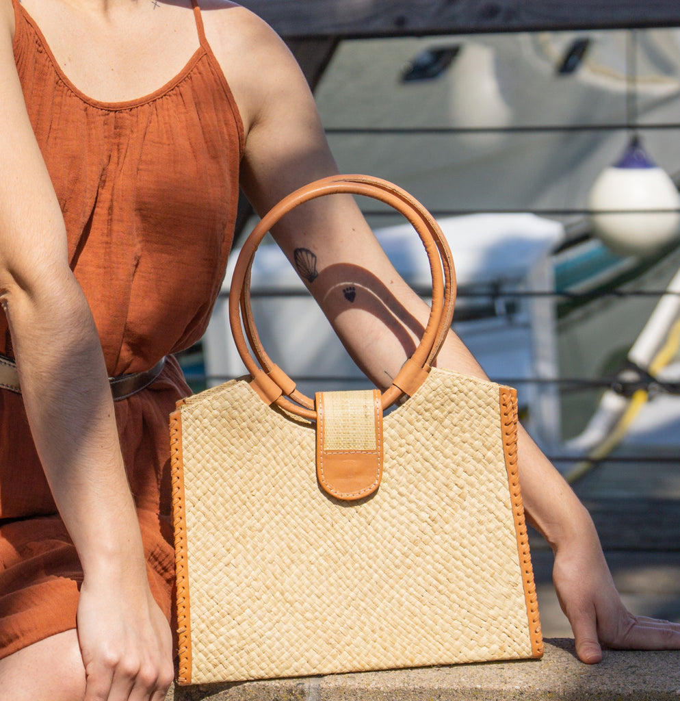 Model wearing Ibiza Natural Straw HandBag with Leather Handles handmade woven natural raffia fiber purse with crosshatch pattern and loomed sides with leather loop handles, woven leather side seam binding, and flap closure - Shebobo