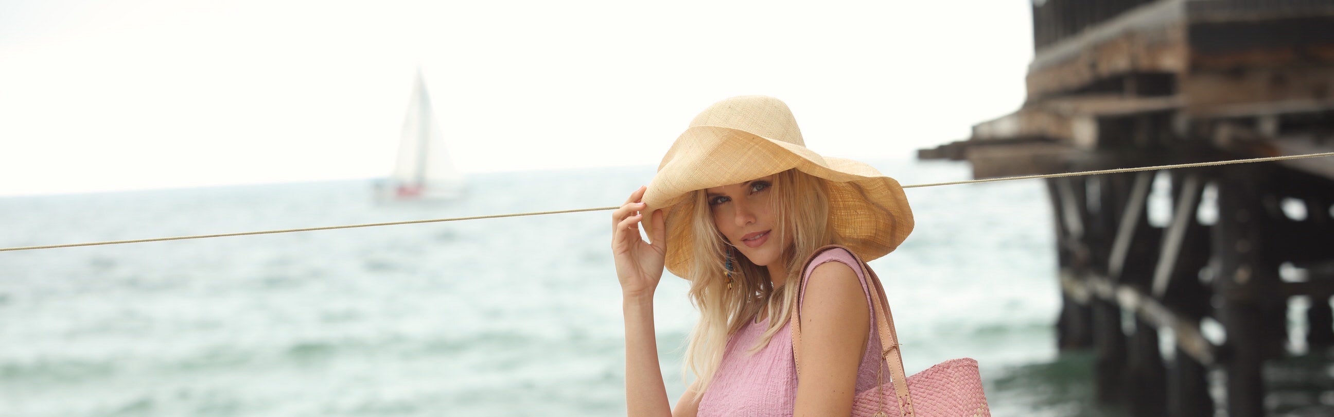 Model wearing Monica 7" wide brim natural packable straw sun hat handmade loomed raffia in a solid hue of natural straw color - Shebobo