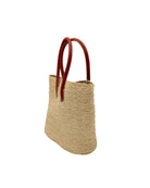 Side view Nomena Braided Straw Basket Handbag handmade braided natural raffia palm fiber in a solid hue of natural straw color woven into concentric horizontal bands of subtle texture spiraling around the bag with leather handles beach bag shoulder bag purse - Shebobo