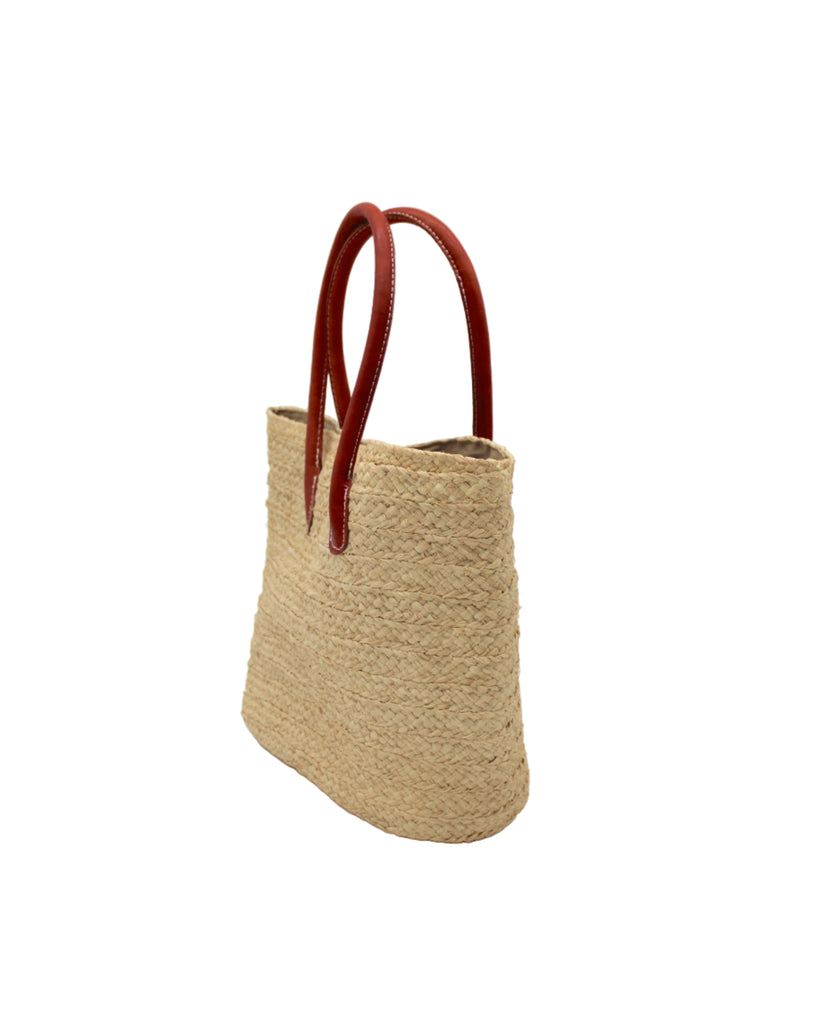 Side view Nomena Braided Straw Basket Handbag handmade braided natural raffia palm fiber in a solid hue of natural straw color woven into concentric horizontal bands of subtle texture spiraling around the bag with leather handles beach bag shoulder bag purse - Shebobo