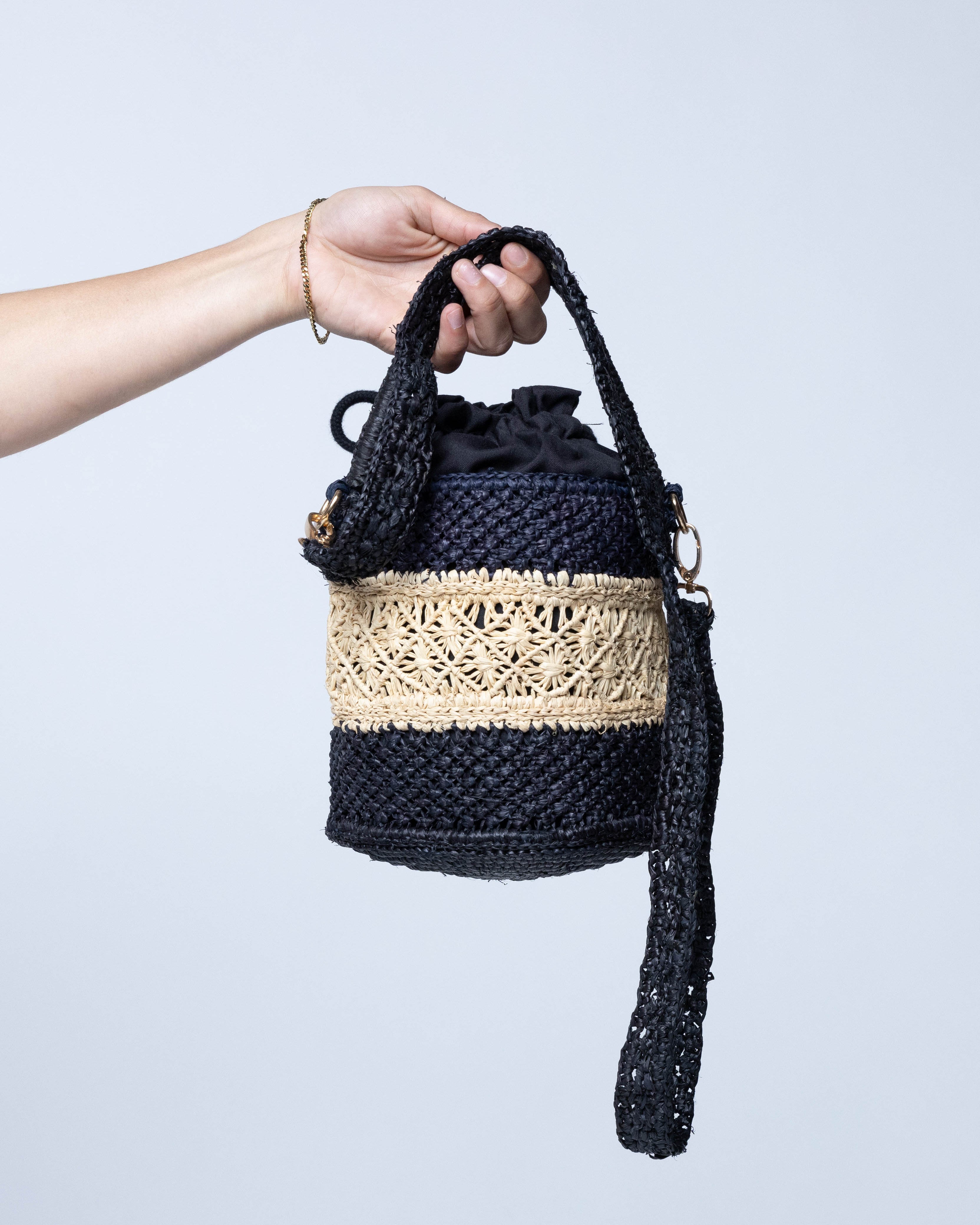 Model wearing Paloma Macrame Diamond & Crochet Straw Bucket Handbag Convertible Crossbody Bag handmade natural raffia palm fiber macrame and crochet in a two tone multicolor of a diamond pattern horizontal band in the center of natural straw color centered with black around the bottom and top of the round bottomed bag in a subtle link crochet texture with detachable shoulder strap - Shebobo