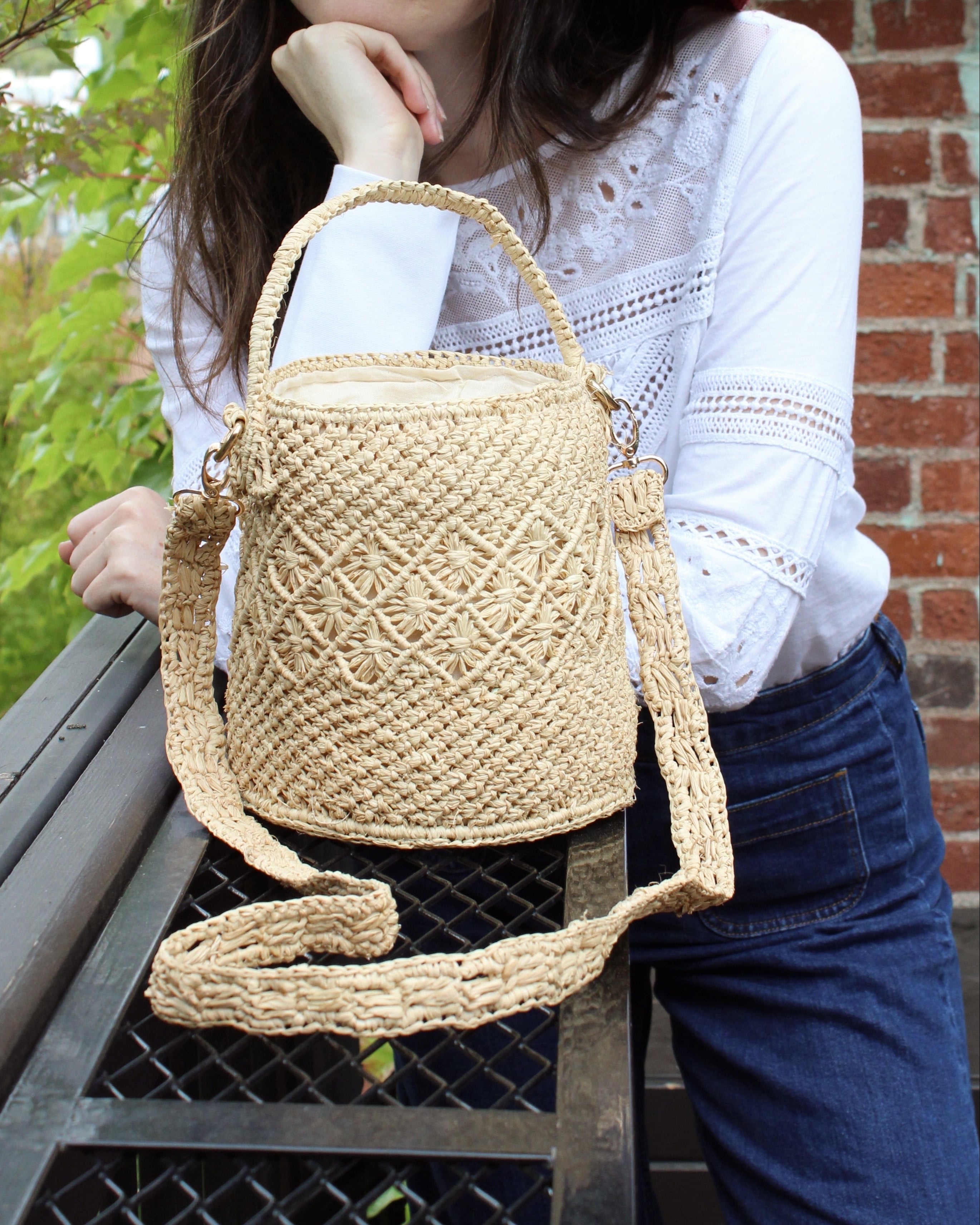 Model wearing Paloma Macrame Diamond & Crochet Straw Bucket Handbag Convertible Crossbody Bag handmade natural raffia palm fiber macrame and crochet in a solid hue of natural straw color round bottomed bag with three even horizontal bands of texture the top and bottom subtle link pattern and the center geometric diagonal starburst or flower in diamond pattern with detachable shoulder strap - Shebobo