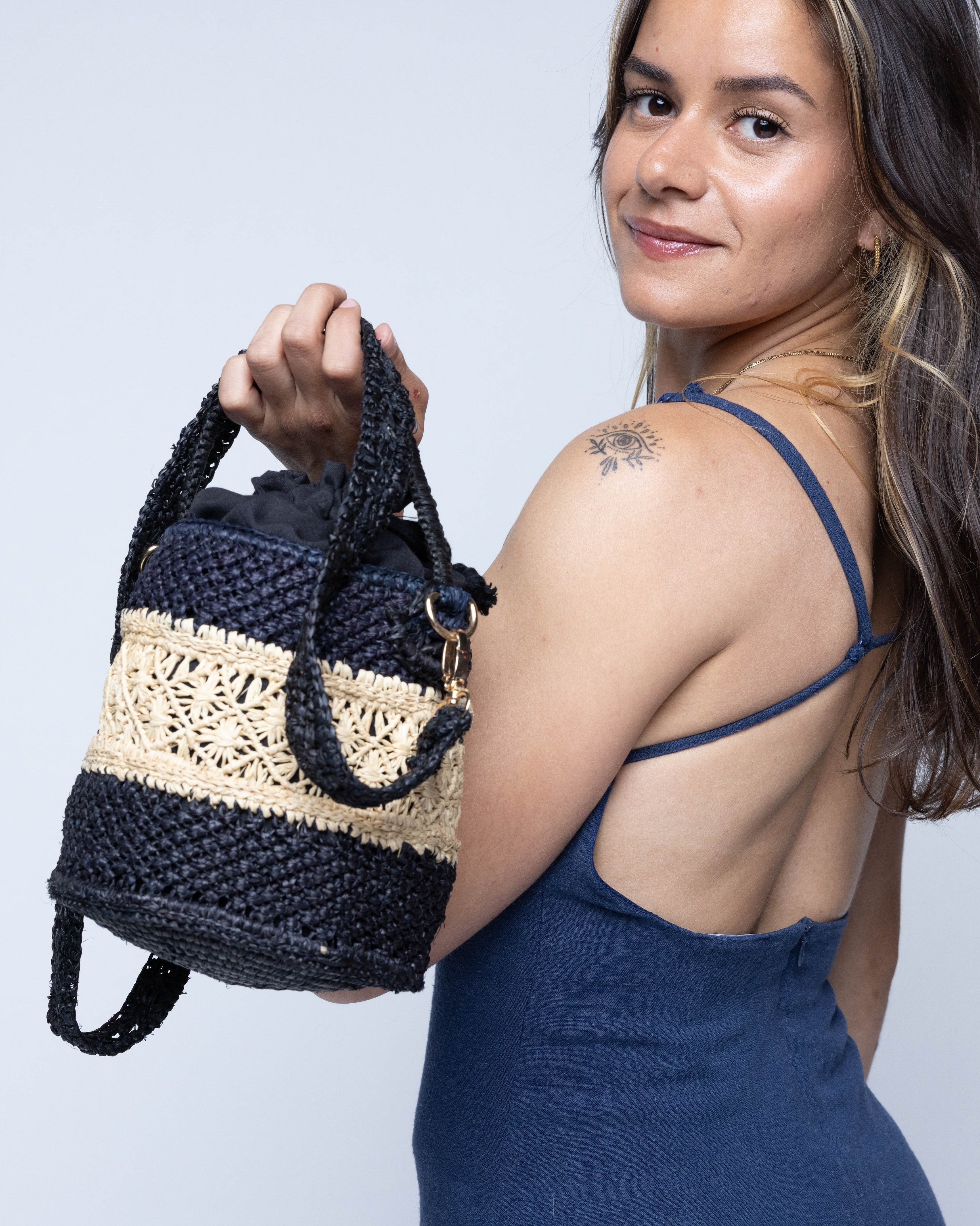 Model wearing Paloma Macrame Diamond & Crochet Straw Bucket Handbag Convertible Crossbody Bag handmade natural raffia palm fiber macrame and crochet in a two tone multicolor of a diamond pattern horizontal band in the center of natural straw color centered with black around the bottom and top of the round bottomed bag in a subtle link crochet texture with detachable shoulder strap - Shebobo