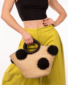 Model wearing Phi Phi Black and Natural Braided Straw Basket with Oversized Raffia Poufs handmade raffia palm fiber braided into a solid hue of natural straw color with three randomly placed black hand-brushed fringe poufs per side for embellishment with matching loop wrap top edging and matching crochet loop/braided handles bag handbag - Shebobo