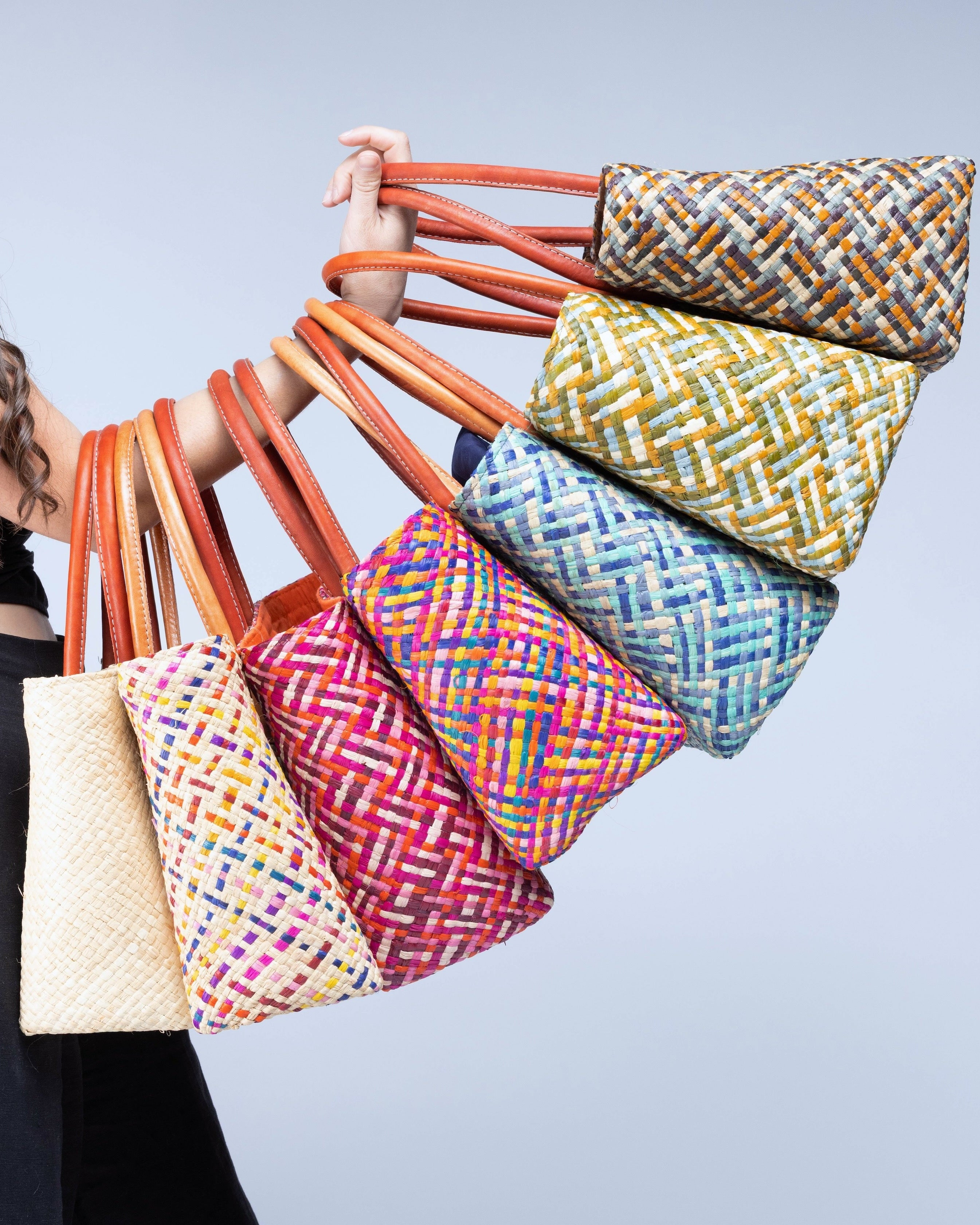 Model wearing multiple color options of Pianina Small Straw Basket Bags handmade from woven natural raffia palm fiber in a multicolor cross weave patterns handbag purse with leather handles - Shebobo