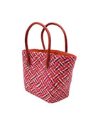 Side view Pianina Passion Multi Small Straw Basket Bag handmade from woven natural raffia palm fiber in a multicolor cross weave pattern of red, light pink, fuchsia, coral, and natural straw color handbag purse with leather handles - Shebobo