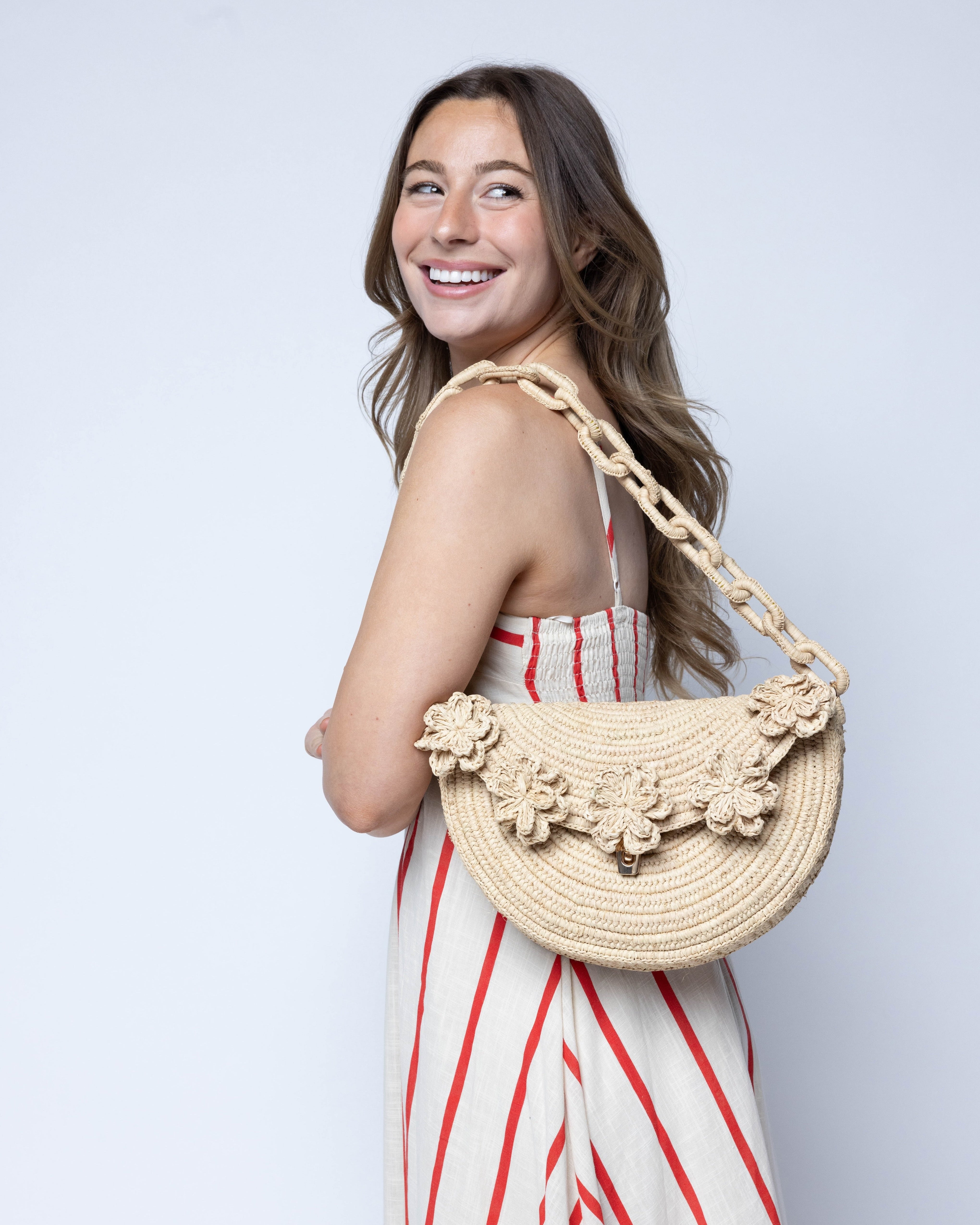 Model wearing Piper Crochet Flower Straw Handbag with Macrame Chain Strap handmade natural raffia palm fiber in a solid hue of natural straw color with delicate 3D floral edge along the front envelope flap style closure of the half moon shaped bag with subtle curved banding and macrame chain shoulder strap purse small bag shoulder bag - Shebobo