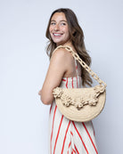Model wearing Piper Crochet Flower Straw Handbag with Macrame Chain Strap handmade natural raffia palm fiber in a solid hue of natural straw color with delicate 3D floral edge along the front envelope flap style closure of the half moon shaped bag with subtle curved banding and macrame chain shoulder strap purse small bag shoulder bag - Shebobo