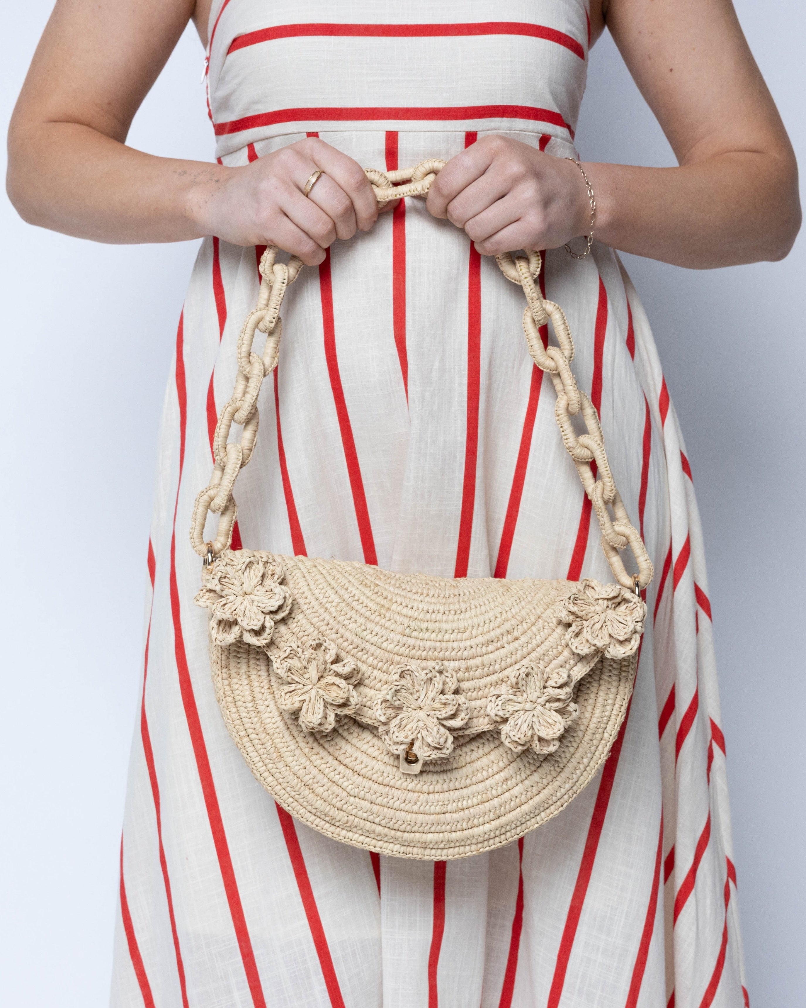 Model wearing Piper Crochet Flower Straw Handbag with Macrame Chain Strap handmade natural raffia palm fiber in a solid hue of natural straw color with delicate 3D floral edge along the front envelope flap style closure of the half moon shaped bag with subtle curved banding and macrame chain shoulder strap purse small bag shoulder bag - Shebobo