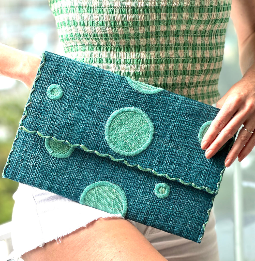 Model wearing Polka Dot Straw Clutch Handbag handmade loomed raffia clutch purse in multisize dot pattern of seafoam green/blue with matching color cross stitch edging on turquoise blue straw color purse - Shebobo