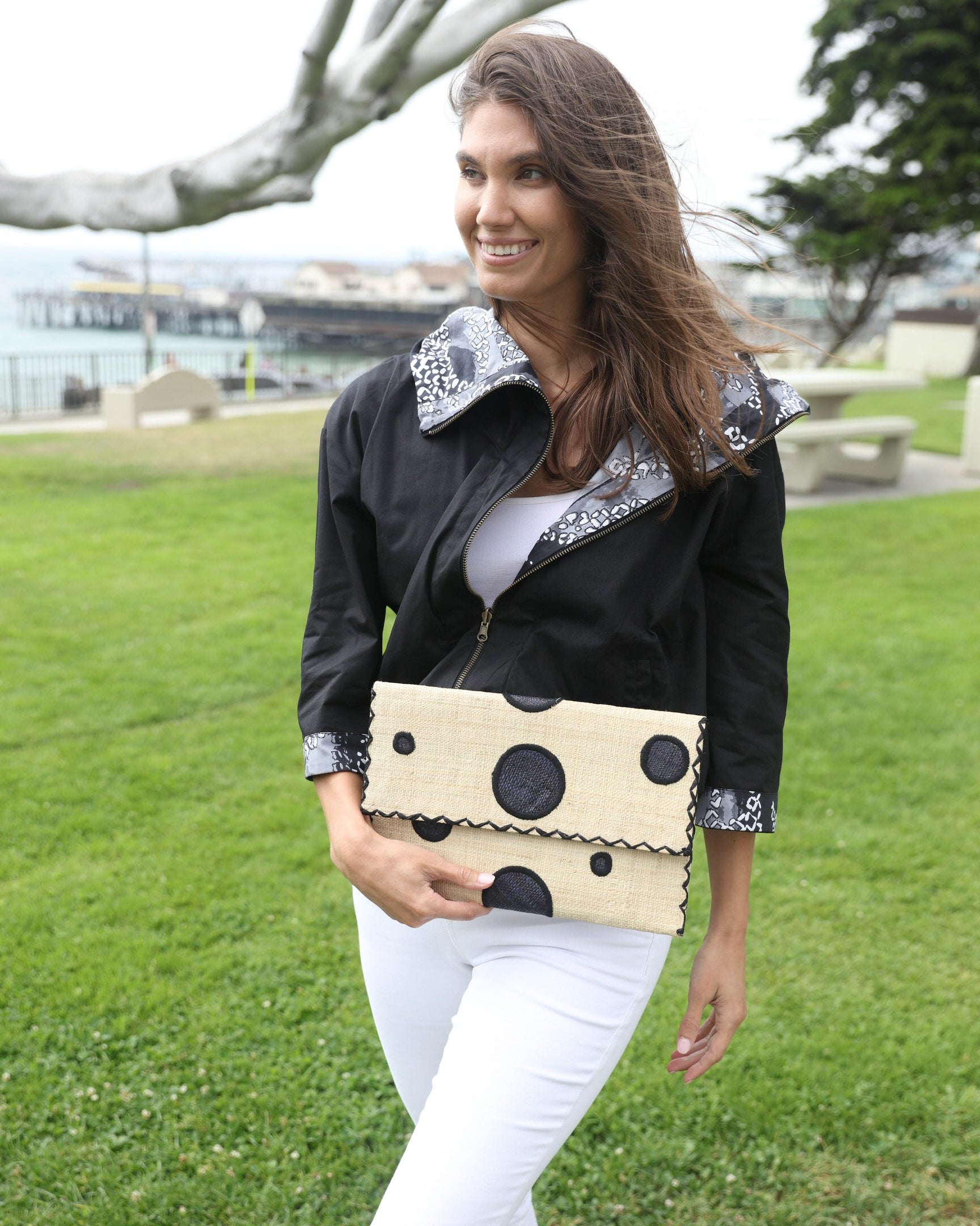 Model wearing Polka Dot Straw Clutch Handbag handmade loomed raffia clutch purse in multisize dot pattern of black dots with matching color cross stitch edging on natural straw color purse- Shebobo