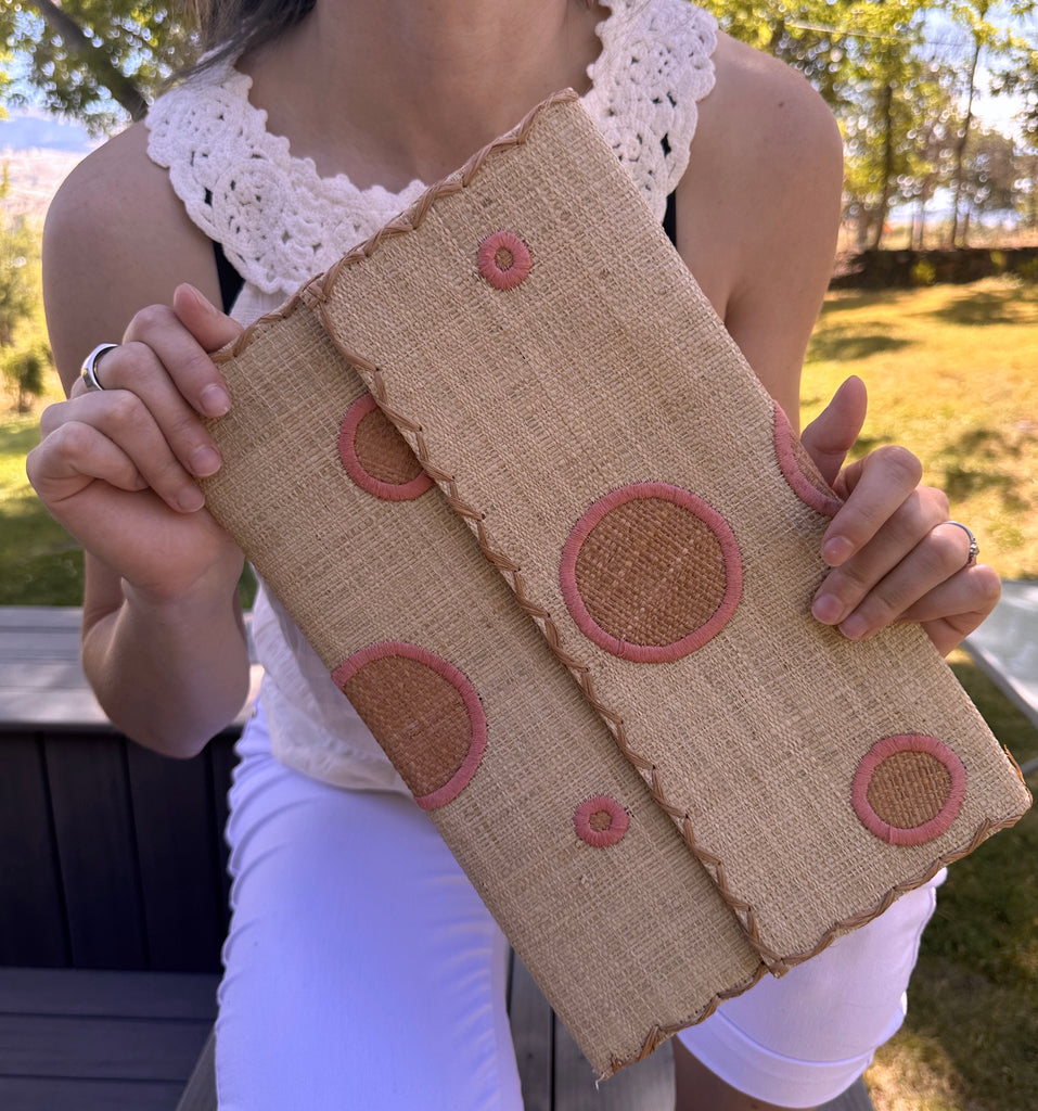 Model wearing Polka Dot Straw Clutch Handbag handmade loomed raffia clutch purse in multisize dot pattern of blush orange/pink dots with matching color cross stitch edging on natural straw color purse- Shebobo