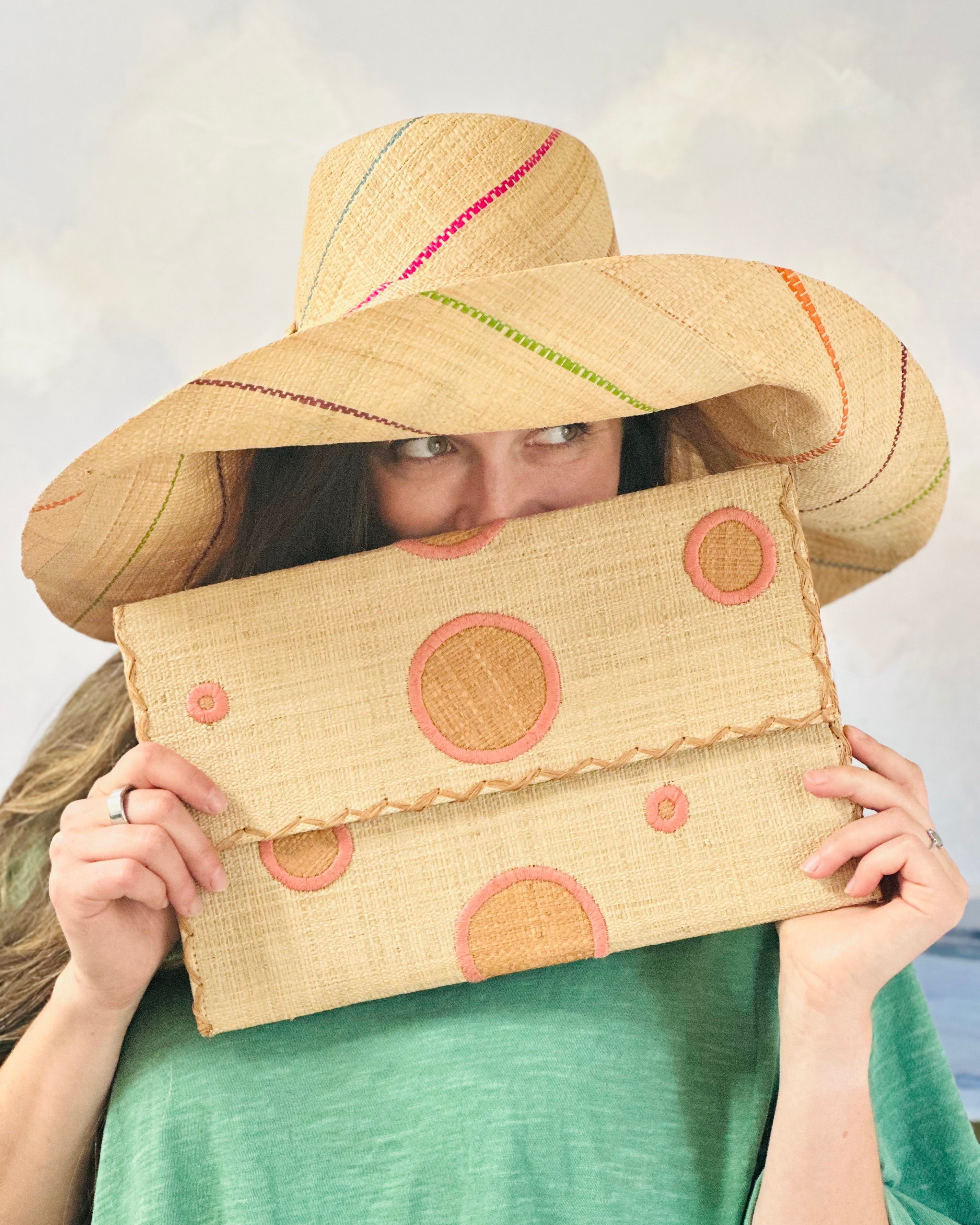 Model wearing Polka Dot Straw Clutch Handbag handmade loomed raffia clutch purse in multisize dot pattern of blush orange/pink dots with matching color cross stitch edging on natural straw color purse- Shebobo (with Monica 5" & 7" Pinstripe Packable Straw Sun Hats)