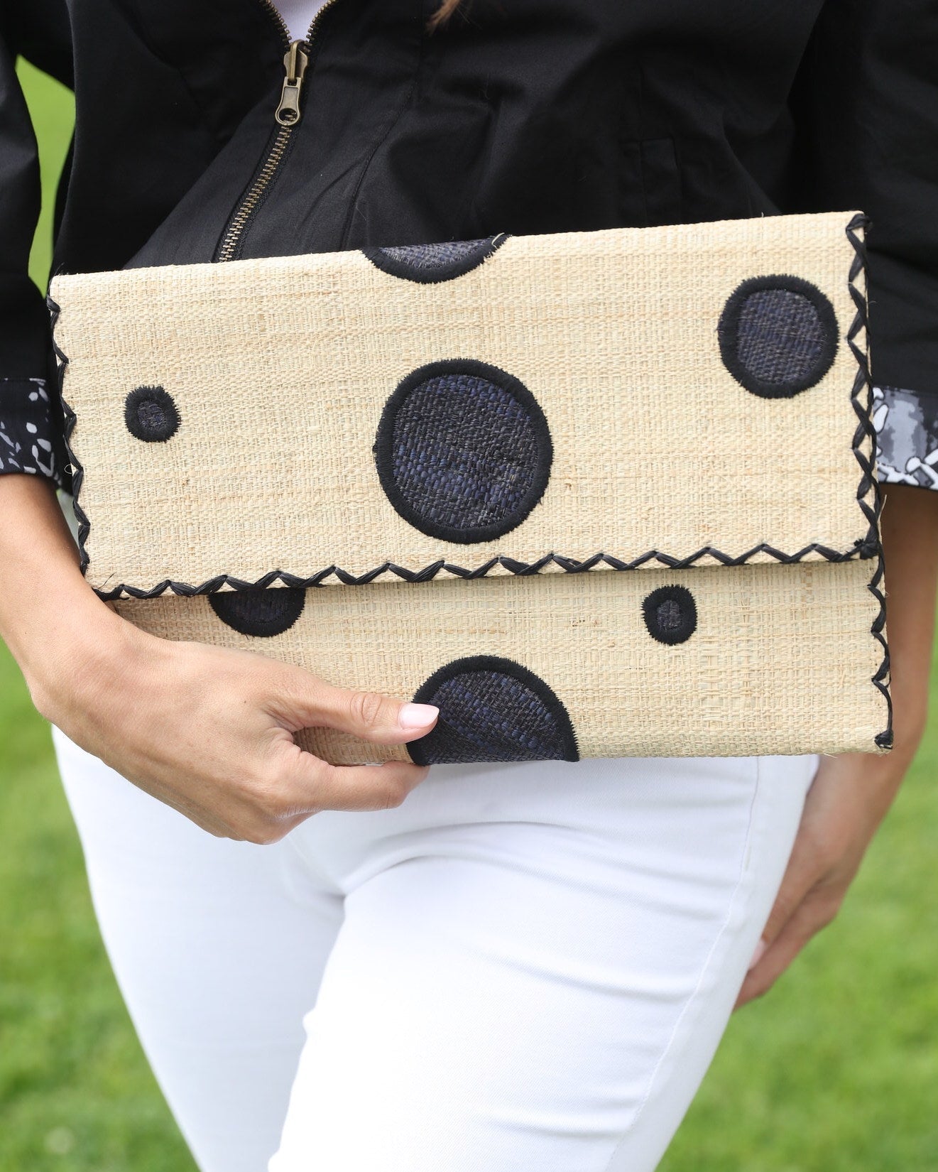 Model wearing Polka Dot Straw Clutch Handbag handmade loomed raffia clutch purse in multisize dot pattern of black dots with matching color cross stitch edging on natural straw color purse- Shebobo