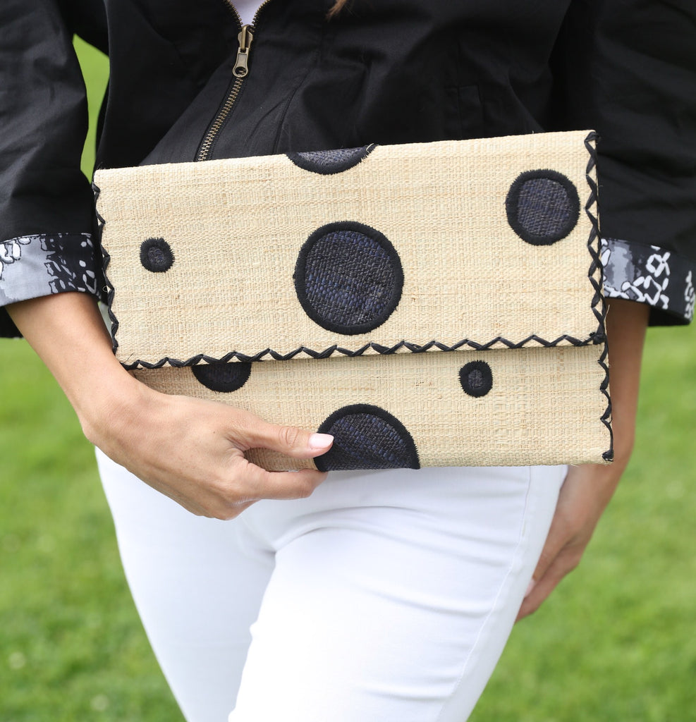 Model wearing Polka Dot Straw Clutch Handbag handmade loomed raffia clutch purse in multisize dot pattern of black dots with matching color cross stitch edging on natural straw color purse- Shebobo