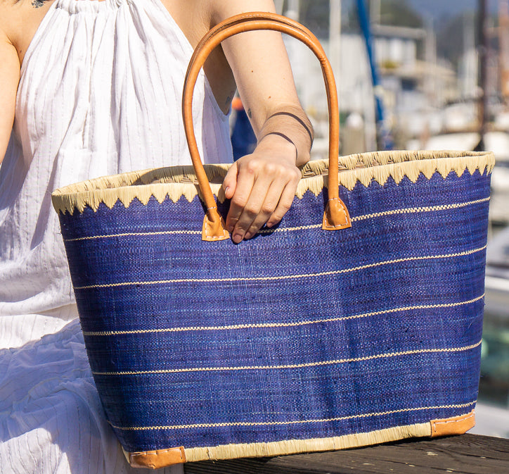 Model wearing Rabat big straw basket bag handmade loomed raffia blue with natural straw color horizontal pinstripe pattern beach bag extra large tote handbag with leather handles - Shebobo