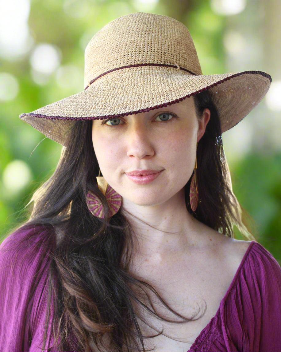 Model wearing 4 inch brim Rachel Crochet Umberwine handmade straw sun hat umberwine bordeaux/claret/deep/dark/red/purple trim woven edge and matching adjustable hat band on natural straw colored raffia hat - Shebobo