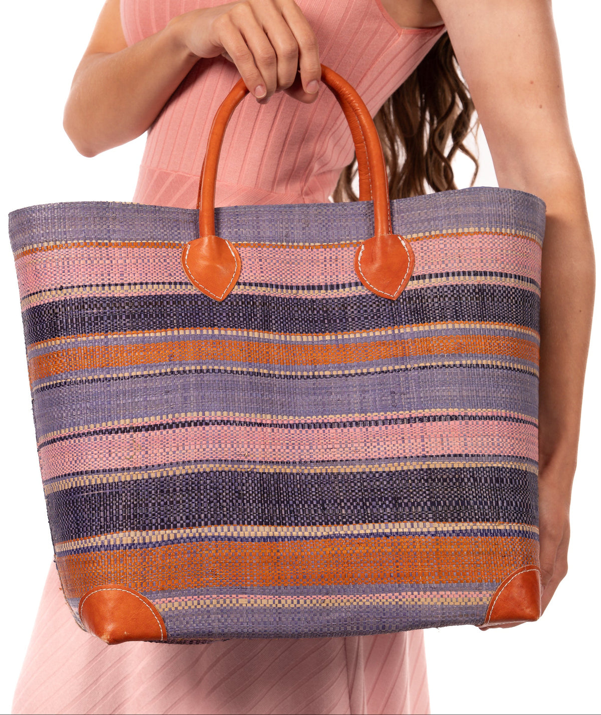 Model Wearing Rayo Stripes Straw Basket Bag Retro Stripe handmade loomed natural raffia palm fiber in a horizontal stripe pattern of multiple widths of natural straw color, denim/retro/light blue, navy/dark blue, baby pink, coral orange/red, etc. handbag with leather handles tote beach bag - Shebobo