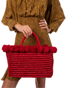 Model wearing Rico Red Crochet Rectangle Straw Basket handmade woven raffia palm fiber in a solid hue of red with horizontal bands of looped texture with matching small raffia pouf pompom top edge and wrapped braid handles small handbag purse - Shebobo
