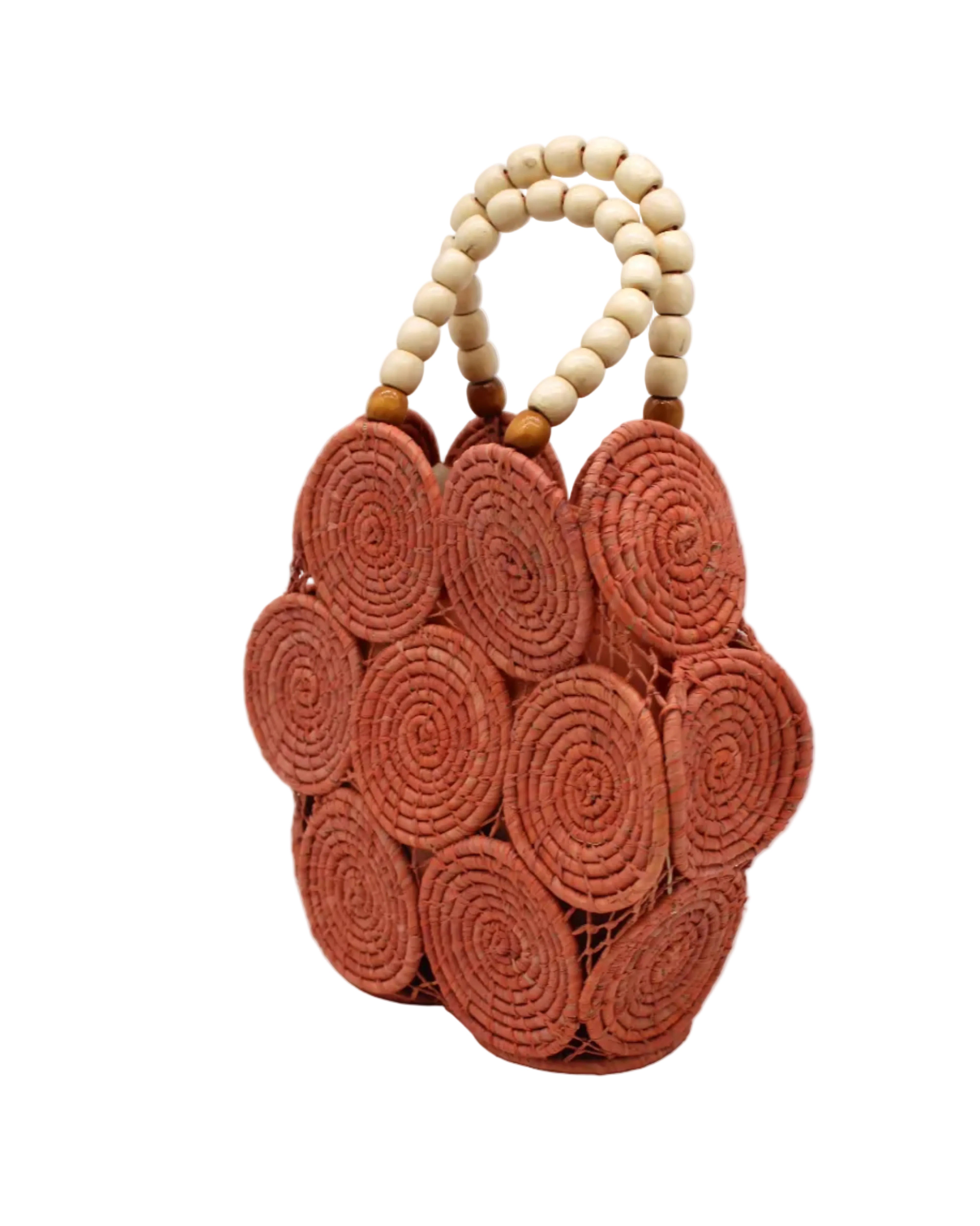 Side view Romy Blush Crochet Disc Straw Handbag with Wooden Bead Handles handmade natural raffia palm fiber in a solid hue of blush orange/pink in a crochet coiled circular flat disc attached together with macrame knot technique with a geometric hexagonal overall shape with seven discs per side two above and below a horizontal row of three per side and a single row comprising the side of the bag with beige carved round wooden beaded handles purse - Shebobo