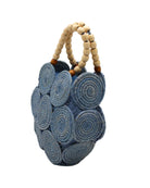 Side view Romy Denim Crochet Disc Straw Handbag with Wooden Bead Handles handmade natural raffia palm fiber in a solid hue of denim retro/light/blue in a crochet coiled circular flat disc attached together with macrame knot technique with a geometric hexagonal overall shape with seven discs per side two above and below a horizontal row of three per side and a single row comprising the side of the bag with beige carved round wooden beaded handles purse - Shebobo
