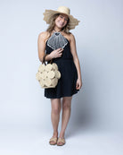 Model wearing Romy Natural Crochet Disc Straw Handbag with Wooden Bead Handles handmade natural raffia palm fiber in a solid hue of natural straw color  in a crochet coiled circular flat disc attached together with macrame knot technique with a geometric hexagonal overall shape with seven discs per side two above and below a horizontal row of three per side and a single row comprising the side of the bag with dark brown carved round wooden beaded handles purse - Shebobo (with Sara Wide Brim Woven Sun Hat)