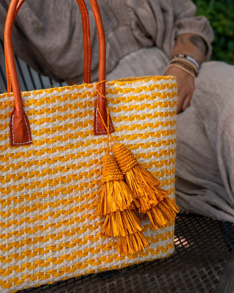 Model wearing Tassel Tie Two Layered Raffia Straw Tiered Tufts Charm Embellishment handmade crochet and brushed natural raffia palm fiber in a single hue layered tuft tassel of Saffron orange/yellow beach bag handbag charm embellishment or party decor - Shebobo