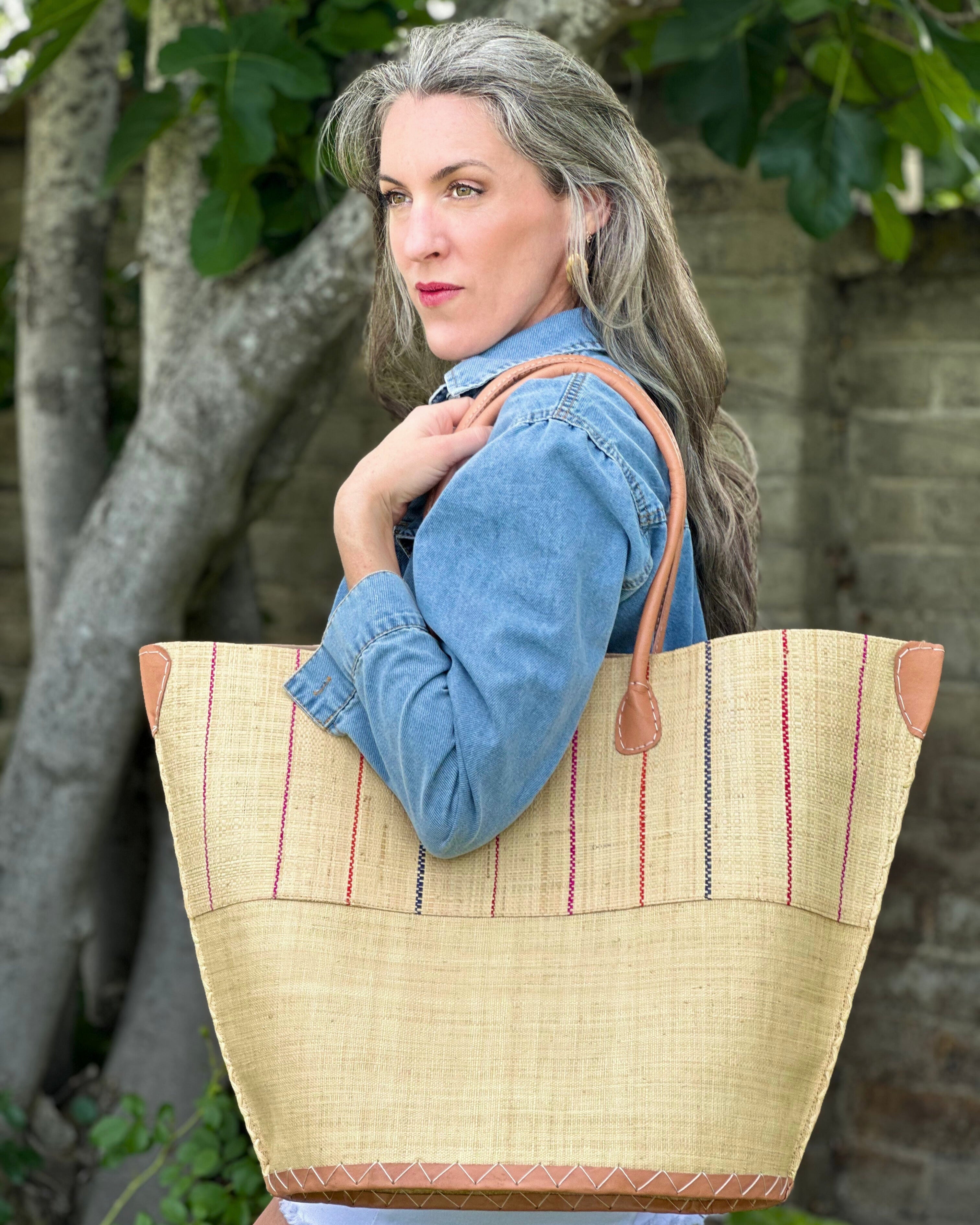 Model wearing Santa Cruz Two Tone Pinstripes Multi Large Straw Tote Bag handmade loomed raffia in a wide stripe of natural straw color with multicolor thin stripes of fuchsia pink, coral red/orange, and navy blue in a vertical pinstripe pattern on the top half and solid natural on the bottom half handbag with leather handles and details beach bag - Shebobo