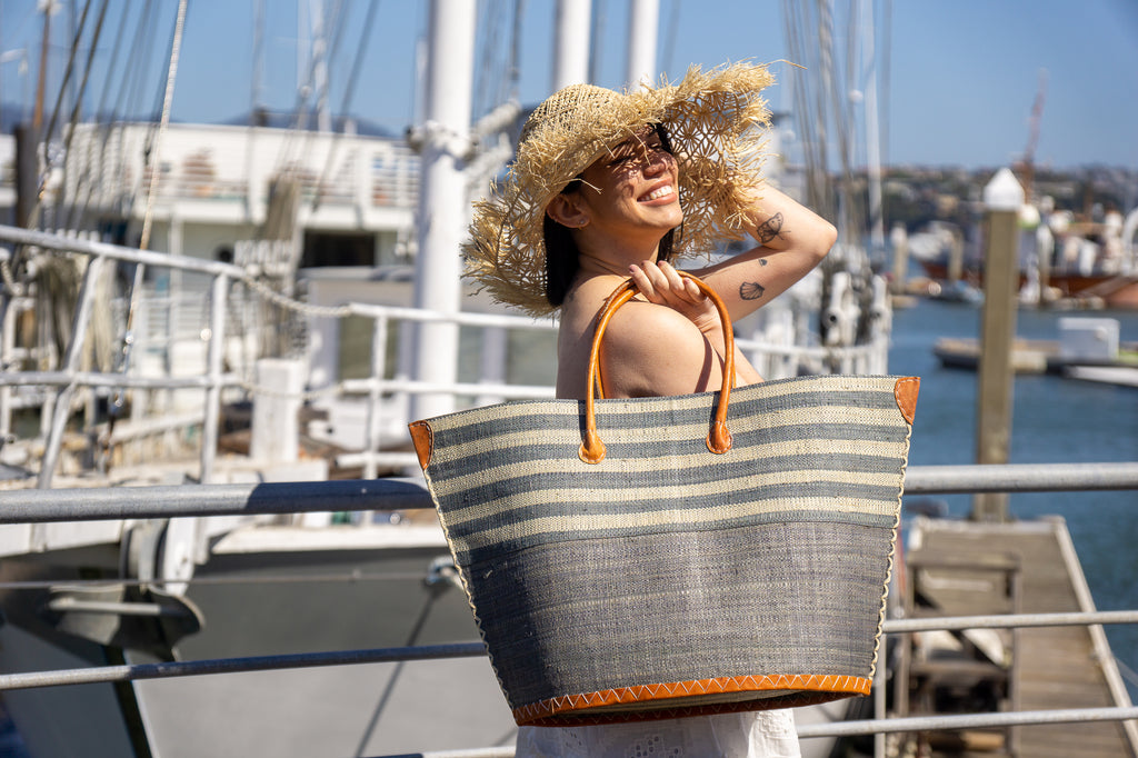 Model wearing Santa Cruz Two Tone Wide Stripes Large Straw Beach Bag Tote Handbag handmade loomed raffia grey and natural horizontal stripes on the top half, and solid grey on the bottom half with leather handles extra large size - Shebobo (with Karin Macrame Straw Sun Hat)