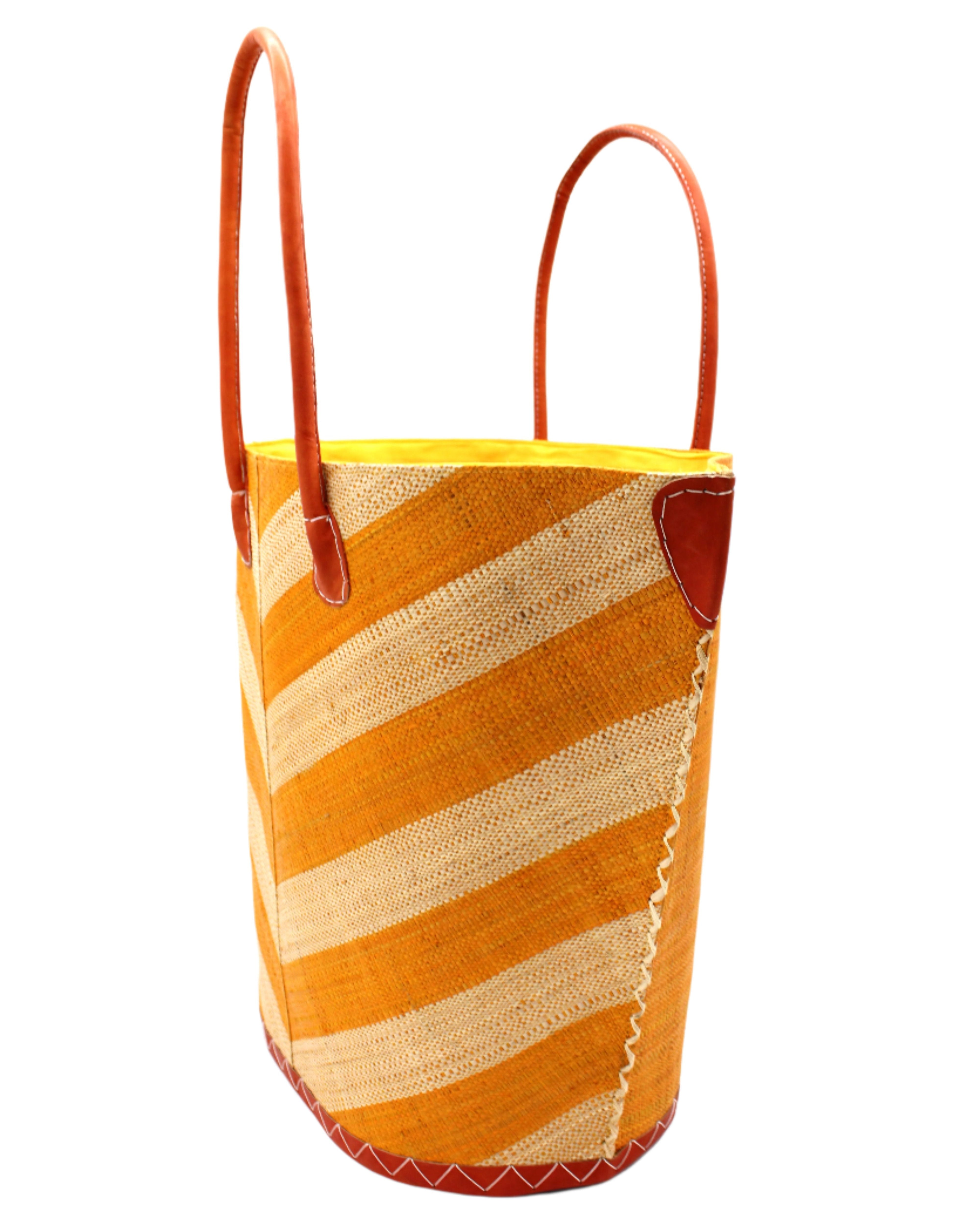 Side view Santa Cruz Wide Stripe Chevron Large Straw Tote Bag handmade loomed raffia palm fiber in a two tone diagonal even width bands of color in a wide stripe chevron pattern of saffron yellow/orange and natural straw color on the front and a matching solid hue on the back with leather accents and handles large shoulder bag - Shebobo