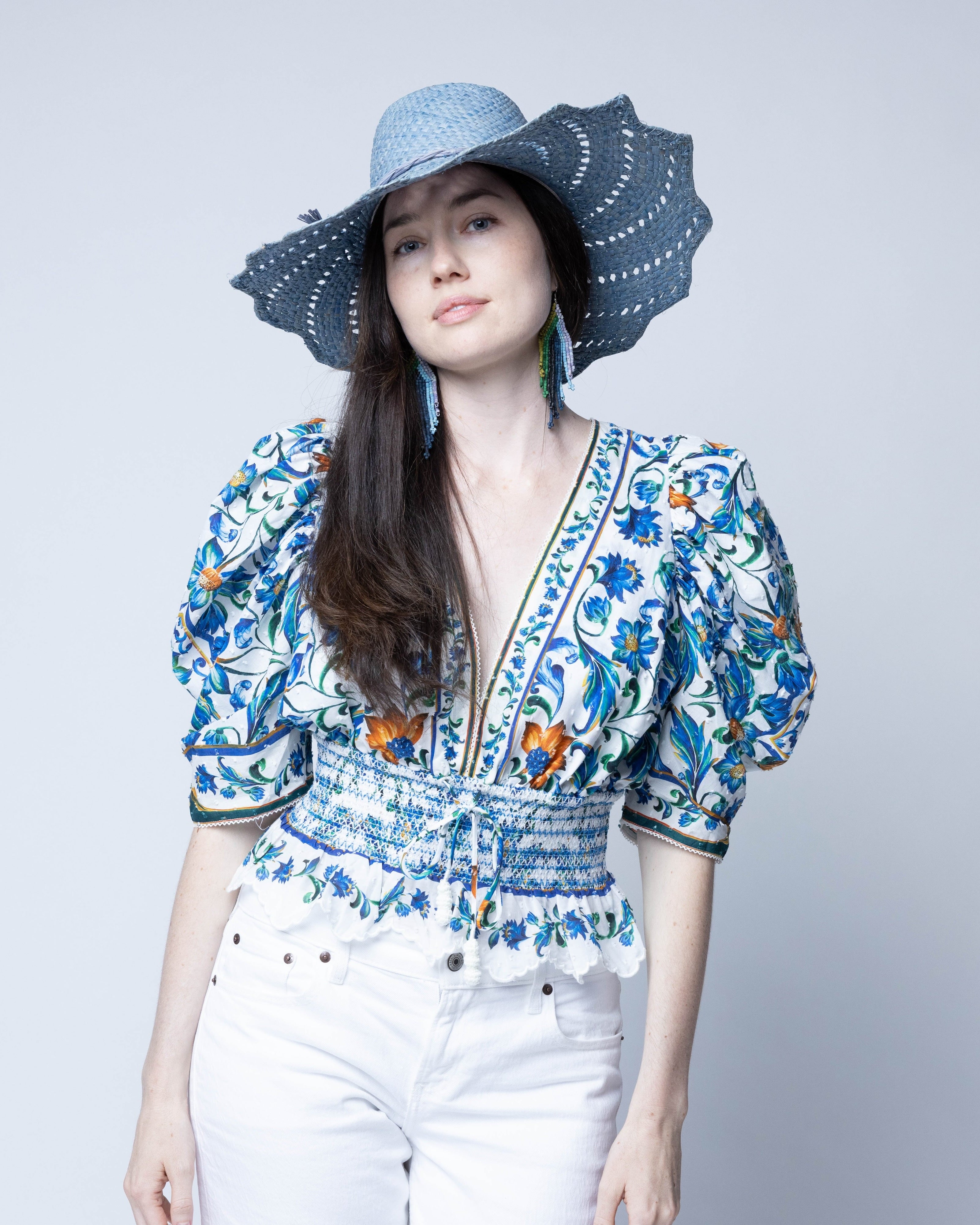 Model wearing Sara 4.5" Brim Woven Straw Sun Hats with Zigzag Edge handmade natural raffia palm fiber in a solid hue of Denim retro/light/blue woven with a subtle crosshatch texture across the crown and spiraling open weave across the brim with matching hat band and zigzag edge - Shebobo