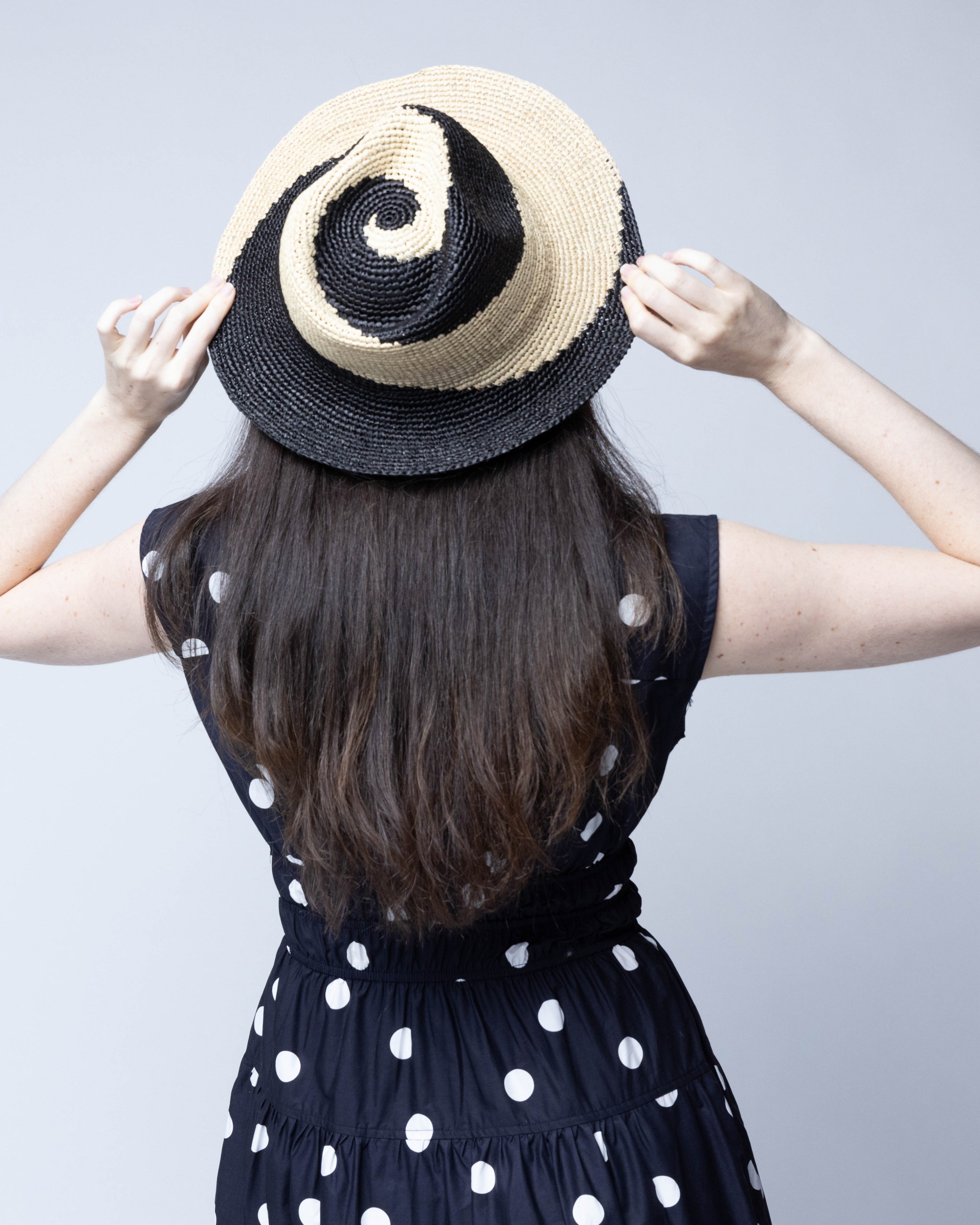 Model wearing Sequoia Black and Natural 3" Brim Swirl Crochet Panama Unisex Straw Hats handmade crochet natural raffia palm fiber in a two tone color swirl design of black and natural straw color spiraling together from wide bands around the brim to a narrow twist at the top of the crown  - Shebobo