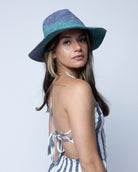 Model wearing Sequoia Denim & Turquoise 3" Brim Swirl Crochet Panama Unisex Straw Hats handmade crochet natural raffia palm fiber in a two tone color swirl design of denim retro/light/blue and turquoise light/blue/green spiraling together from wide bands around the brim to a narrow twist at the top of the crown  - Shebobo
