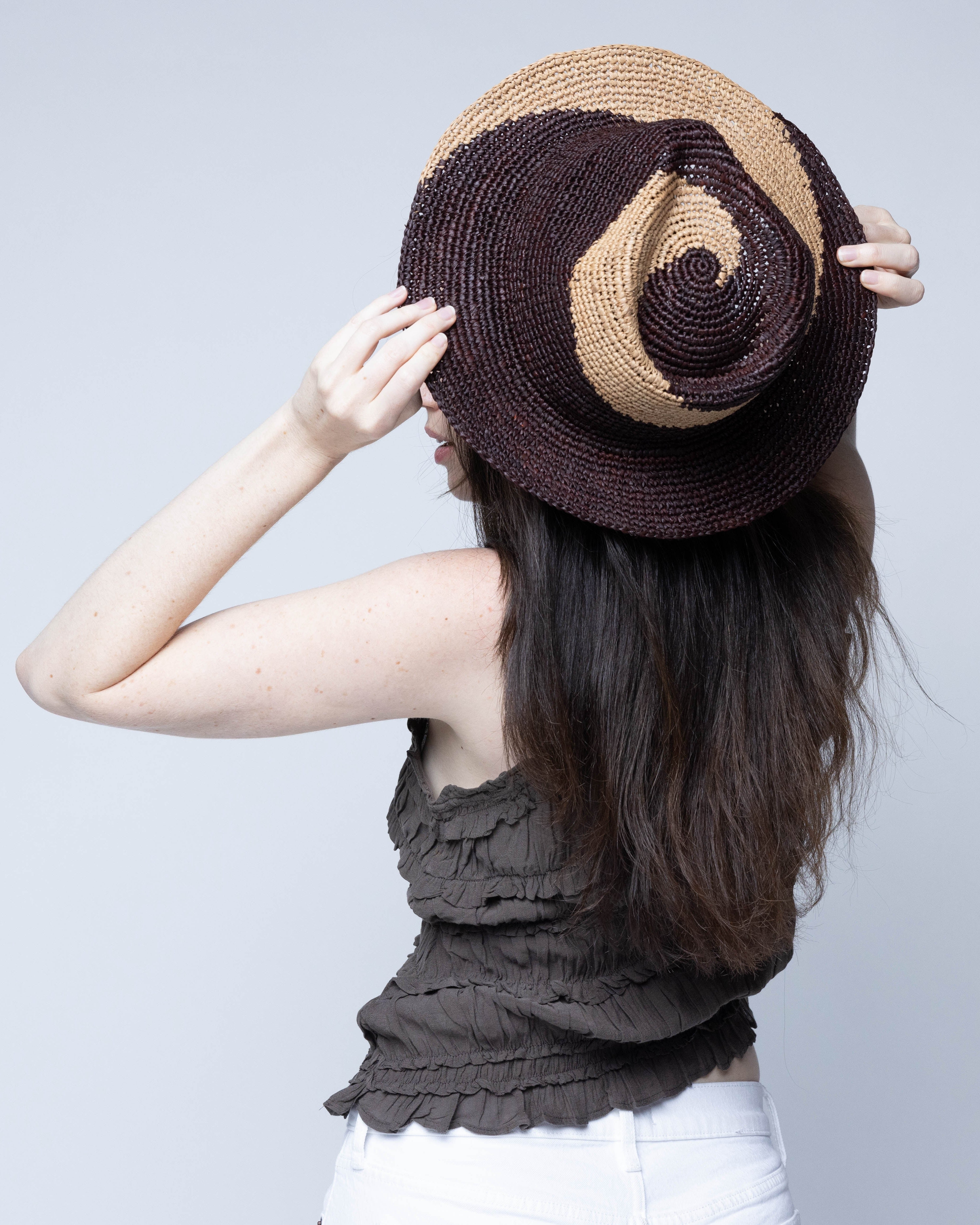 Model wearing Sequoia Cappuccino & Espresso 3" Brim Swirl Crochet Panama Unisex Straw Hats handmade crochet natural raffia palm fiber in a two tone color swirl design of cappuccino tea/light/brown and espresso dark/chocolate/brown spiraling together from wide bands around the brim to a narrow twist at the top of the crown  - Shebobo