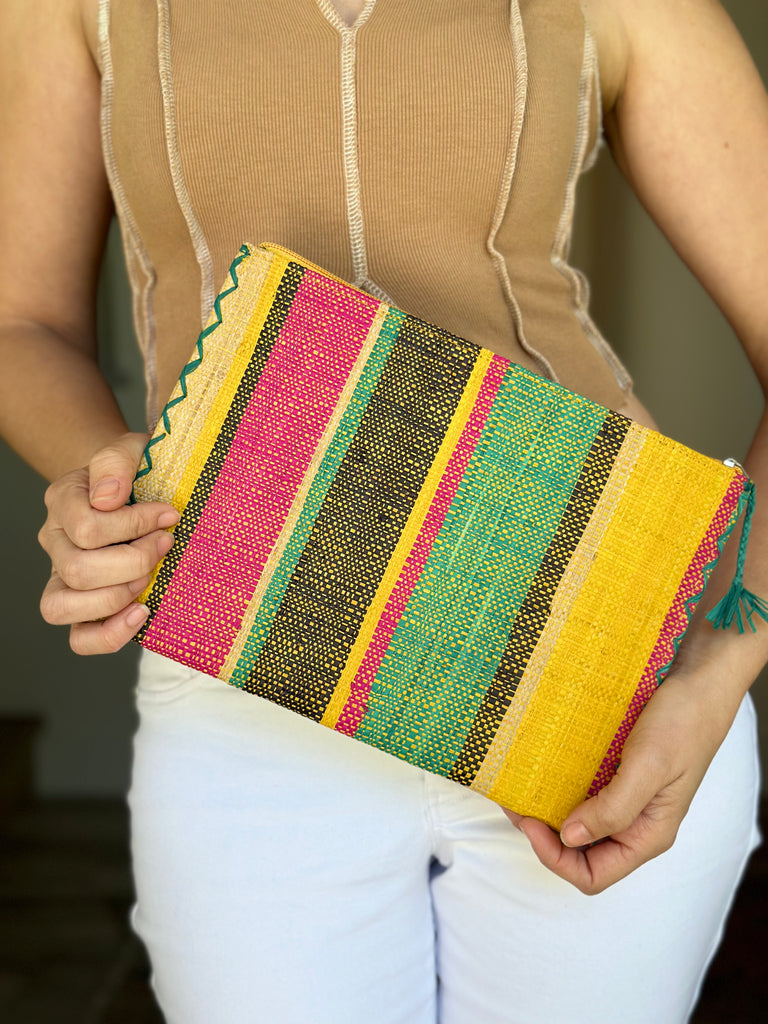 Model wearing Set of 3 Nesting Zippered Straw Clutches Carmalita Multicolor Stripe Pattern handmade loomed raffia in multiple widths of vertical stripes in turquoise, black, fuchsia, and saffron with matching zipper and braided zipper pull with cross stitch edging in three sizes of small, medium, and large - Shebobo