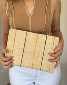 Model wearing Set of 3 Neutrals on Natural straw color Nesting Zippered Straw Clutches Pinstripe Pattern handmade loomed raffia in wide vertical bands of natural with multicolor narrow bands of cinnamon/tobacco/brown, black, and blush with matching zipper and braided zipper pull with cross stitch edging in three sizes of small, medium, and large - Shebobo