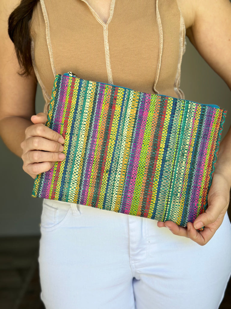 Model wearing Set of 3 Nesting Zippered Straw Clutches Turquoise Stripe Multicolor Stripe Pattern handmade loomed raffia in multiple widths of vertical stripes in natural, orange, turquoise, saffron, seafoam, red, fuchsia pink, etc. with matching turquoise zipper and braided zipper pull with cross stitch edging in three sizes of small, medium, and large - Shebobo