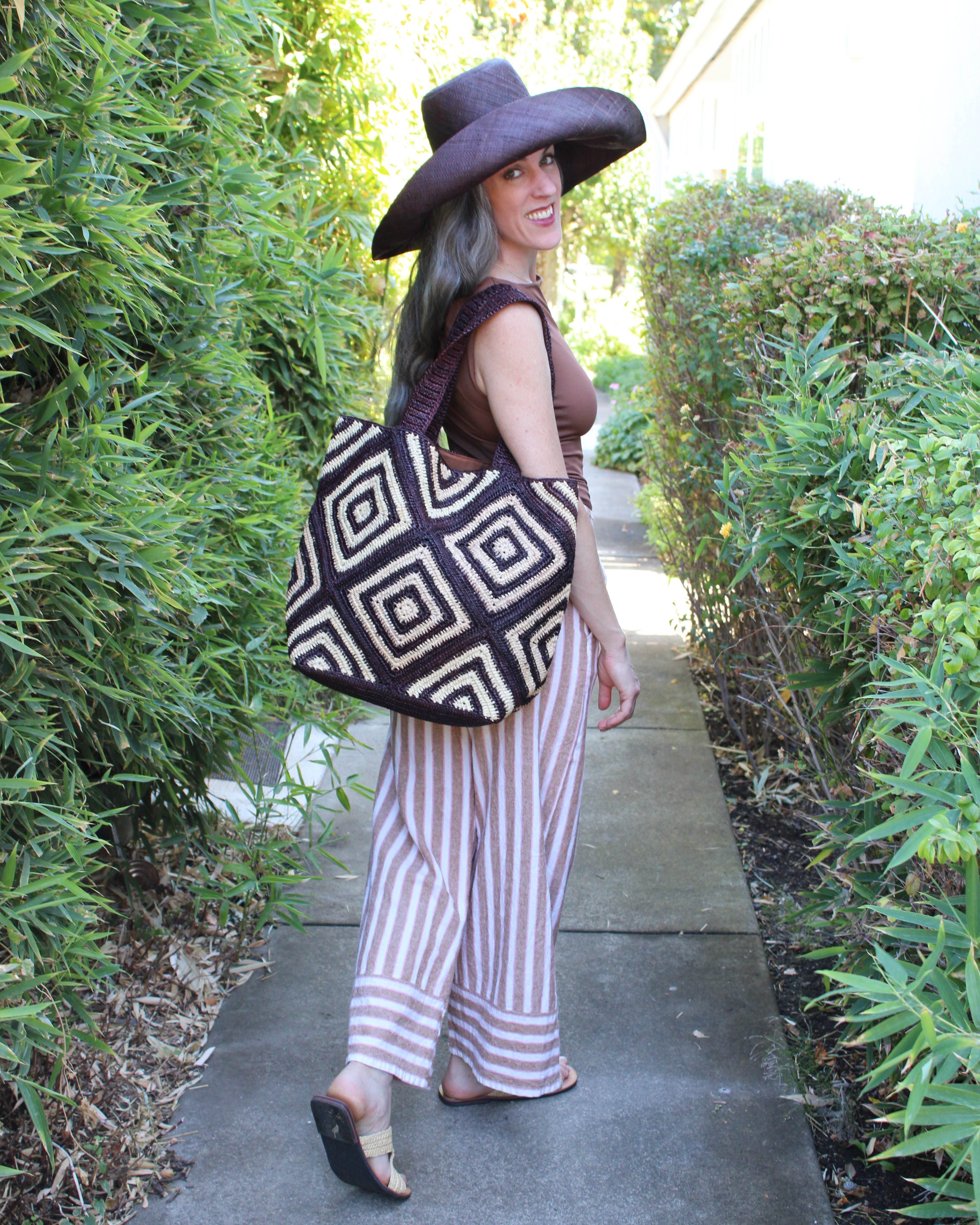 Model wearing Seychelle Mocha and Natural Diamond Pattern Crochet Straw Basket Handbag handmade natural raffia palm fiber in a two tone multicolor geometric diamond pattern with aternating Mocha chocolate/dark/brown and natural straw colored diamonds that make a diagonal bullseye pattern with matching crochet handles beach bag tote purse - Shebobo (with Monica Wide Brim Solid Color Packable Straw Sun Hats)