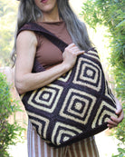 Model wearing Seychelle Mocha and Natural Diamond Pattern Crochet Straw Basket Handbag handmade natural raffia palm fiber in a two tone multicolor geometric diamond pattern with aternating Mocha chocolate/dark/brown and natural straw colored diamonds that make a diagonal bullseye pattern with matching crochet handles beach bag tote purse - Shebobo